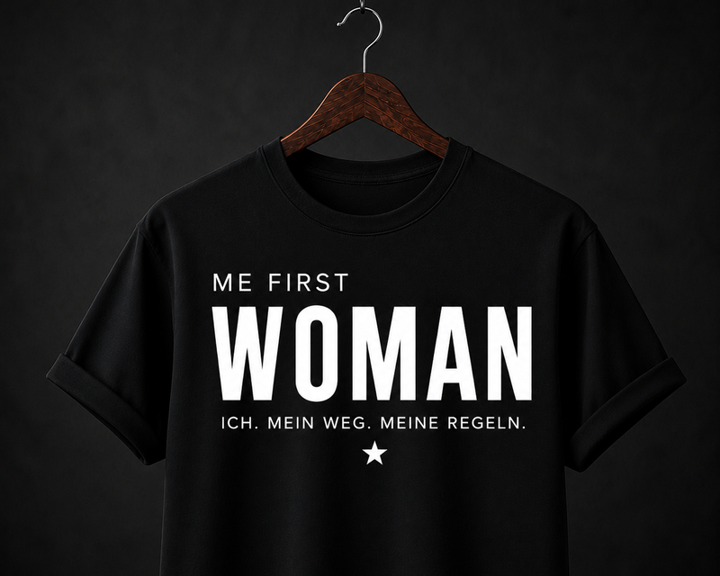 Schwarzer Damen-Statement-Shirt mit weißem ME FIRST WOMAN Schriftzug auf dunklem Hintergrund.
