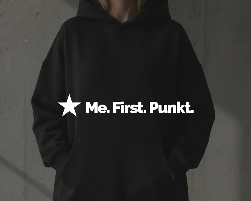 Schwarzer Damen-Hoodie in moderner architektonischer Umgebung vor Betonwand, Hände in Taschen, ohne sichtbares Gesicht.