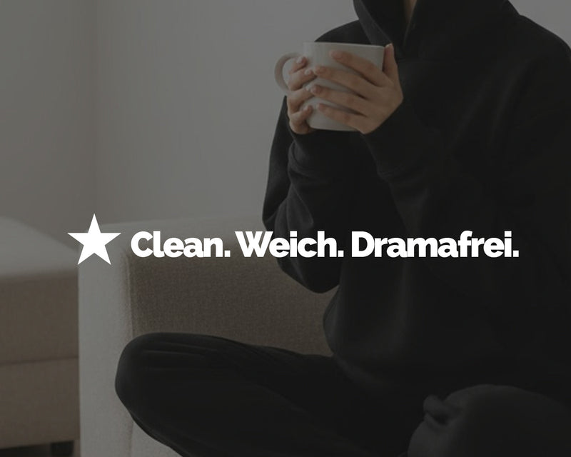 Frau im schwarzen Hoodie sitzt entspannt auf einem hellen Sofa und hält eine Tasse. Bildausschnitt ohne Gesicht.