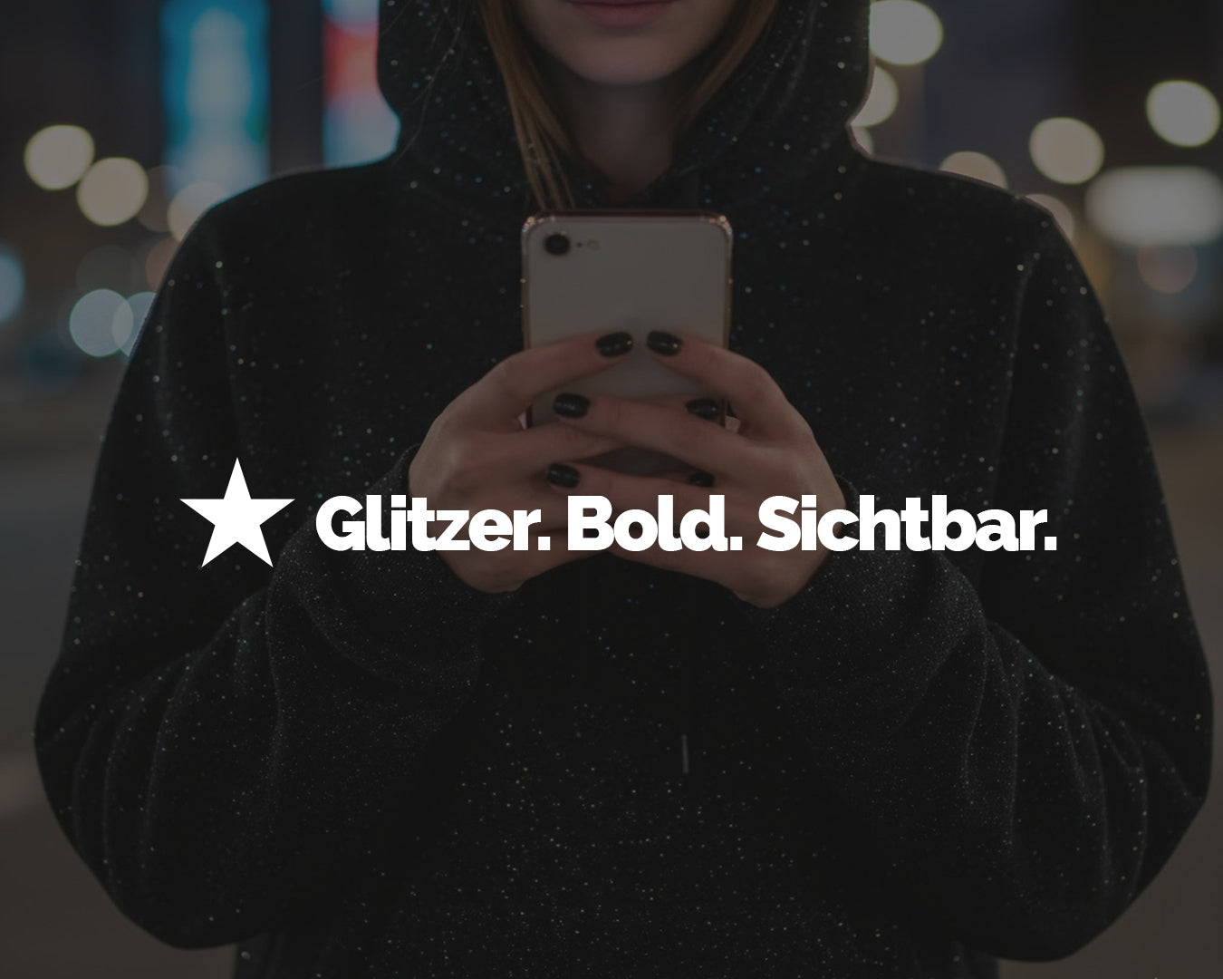 Frau in schwarzem Hoodie mit Glitzer-Effekt, im Dunkeln mit Smartphone in der Hand, Bildausschnitt ohne Gesicht.