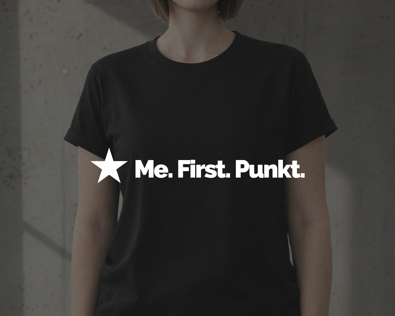 Frau trägt schwarzes First-Me Statement-Shirt mit Roll-up-Ärmeln – minimalistisches Design, selbstbewusste Haltung, klare Botschaft.