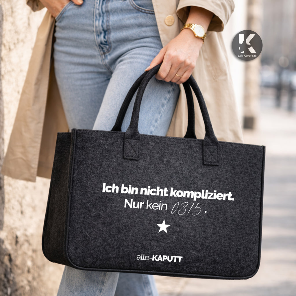 Schwarze Filztasche mit Statement „Ich bin nicht kompliziert. Nur kein 0815.“ im Streetstyle, getragen von einer Frau mit Trenchcoat, Jeans und weißen Sneakern.