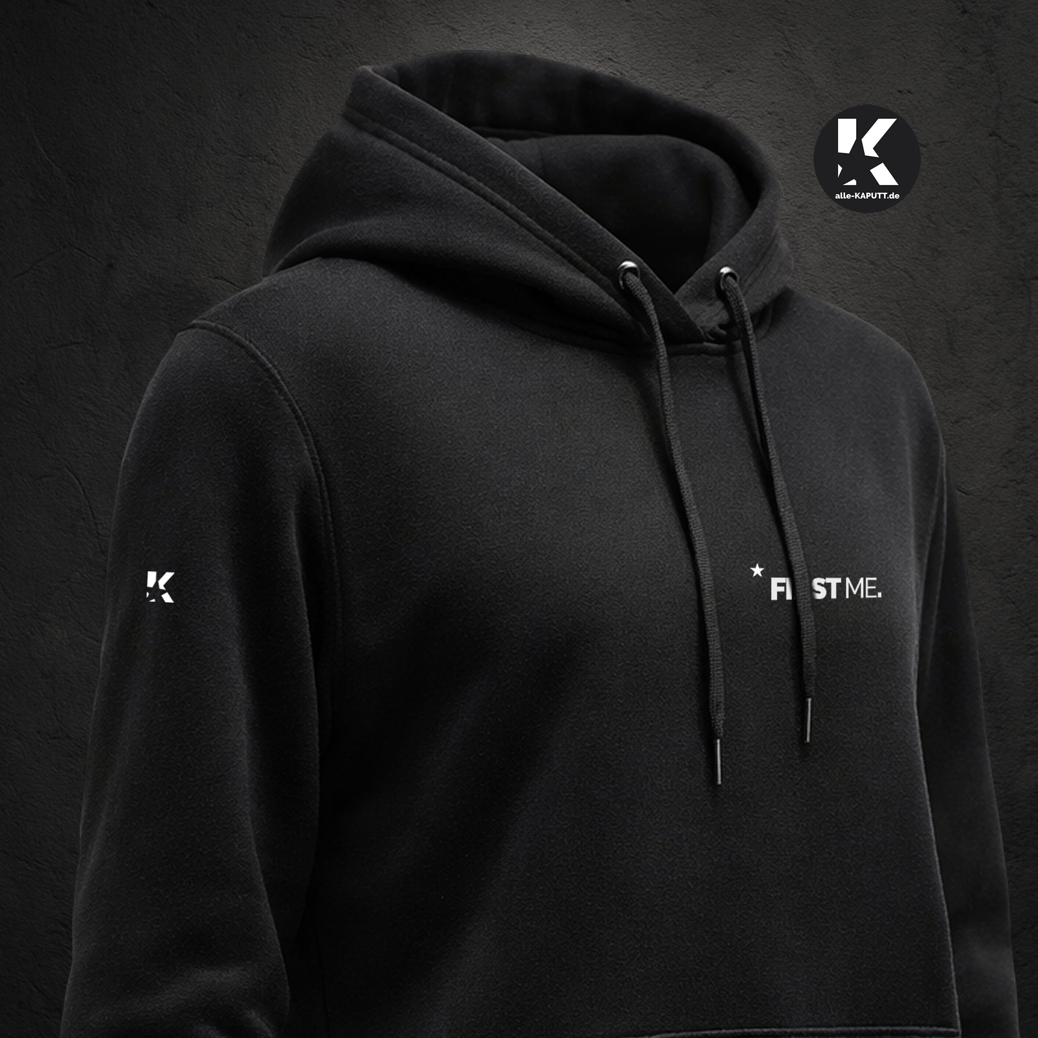 Schräg aufgenommene Vorderansicht eines schwarzen Hoodies mit Statement „FIRST ME.“ und K-Stern am Ärmel aus der First-Me-Collection von alle-KAPUTT