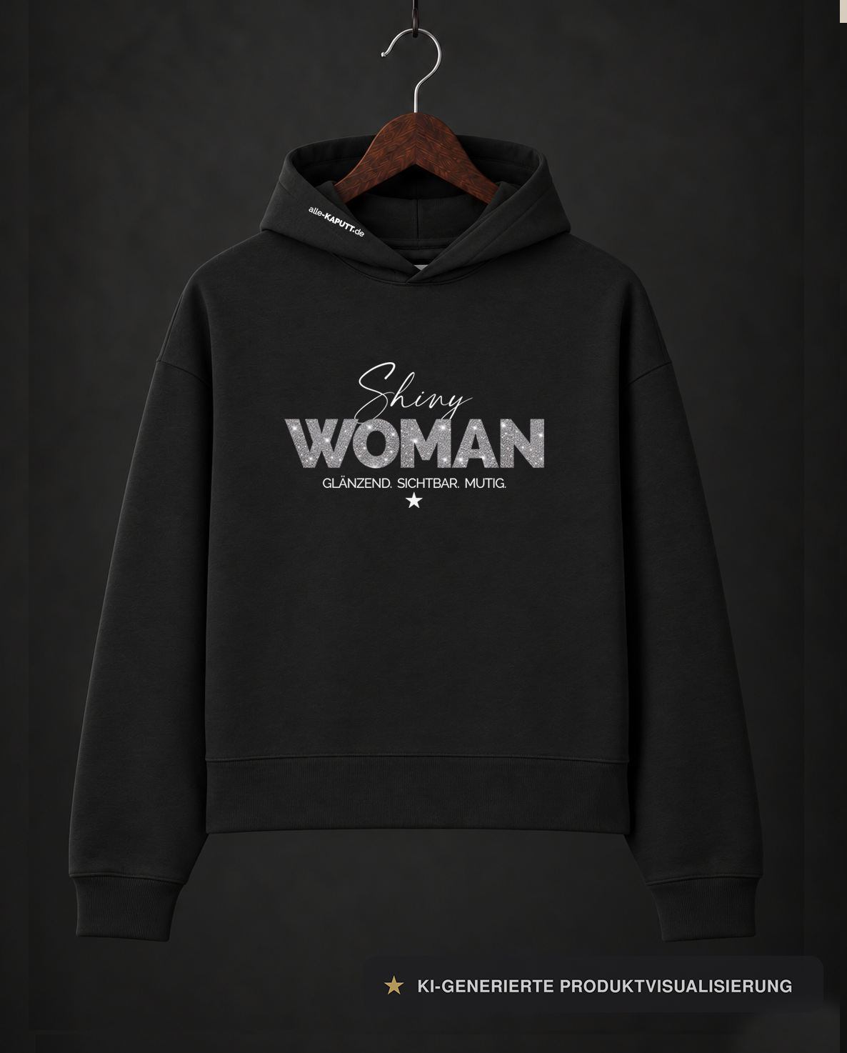 Schwarzer SHINY WOMAN Cropped-Hoodie von alle-KAPUTT mit silbernem Glitzerprint und dem Claim „GLÄNZEND. SICHTBAR. MUTIG.“ am Holzkleiderbügel.