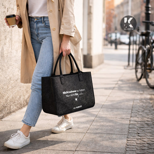 Schwarze Filztasche mit dem Statement „Nicht schwer zu haben. Nur nicht für jeden.“ getragen von einer Frau im Trenchcoat auf der Straße – alle-KAPUTT Lifestyle Bild